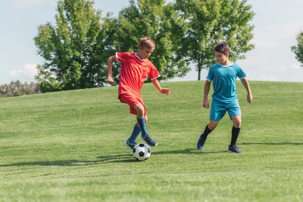 Mignons amis en vêtements de sport jouer au football sur l'herbe verte dans le parc — Photo de stock