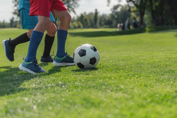 Vue recadrée des enfants jouant au football sur l'herbe — Photo de stock