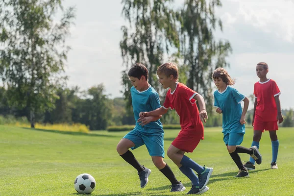 Quatro crianças multiculturais jogando futebol na grama — Fotografia de Stock