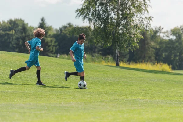 Freunde in blauer Sportbekleidung spielen Fußball auf grünem Rasen — Stockfoto