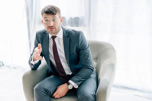 Hombre de negocios guapo en traje y gafas hablando y sentado en sillón - foto de stock