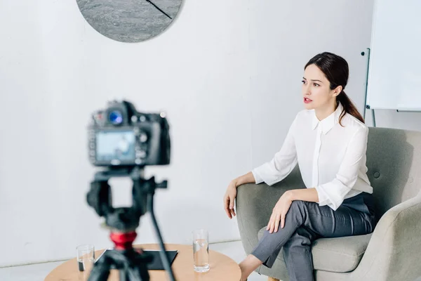 Enfoque selectivo de periodista en ropa formal hablando y sentado en sillón - foto de stock