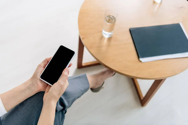 Ausgeschnittene Ansicht eines Journalisten, der im Büro sitzt und Smartphone mit Kopierplatz hält — Stockfoto