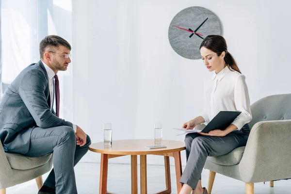 Seitenansicht eines gutaussehenden Geschäftsmannes in Anzug und Brille im Gespräch mit einem Journalisten — Stock Photo