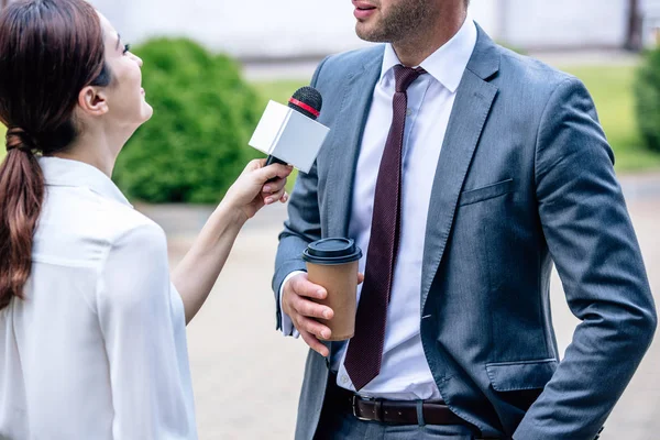 Journalist holding microphone and talking with businessman in formal wear — Stock Photo