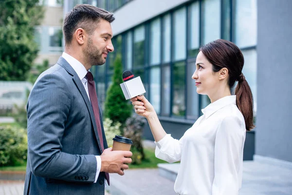 Periodista sosteniendo micrófono y hablando con hombre de negocios en ropa formal - foto de stock