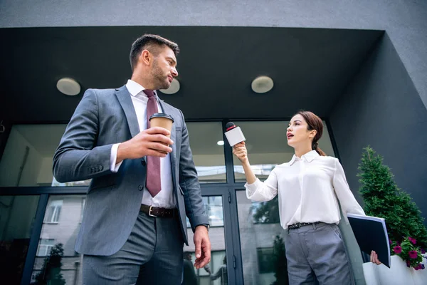 Periodista sosteniendo micrófono y hablando con hombre de negocios en ropa formal - foto de stock