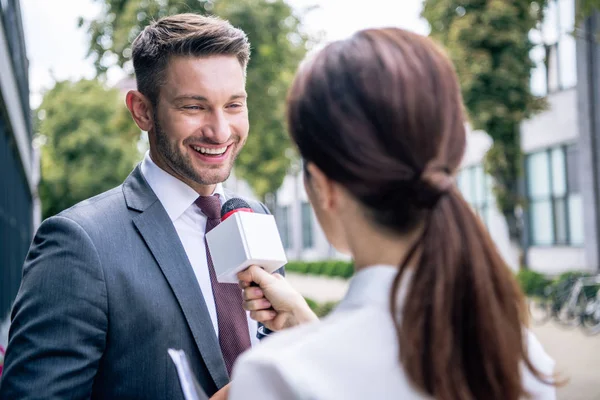 Journalist holding microphone and talking with businessman in formal wear — Stock Photo