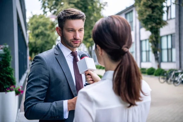 Journalist holding microphone and talking with businessman in formal wear — Stock Photo