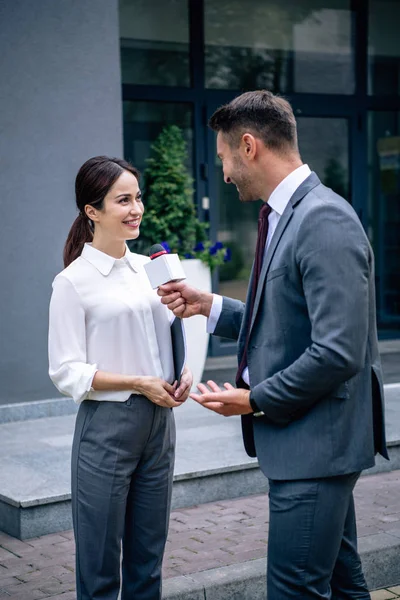 Journalist holding microphone and talking with businesswoman in formal wear — Stock Photo