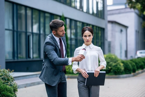 Periodista sosteniendo micrófono y hablando con empresaria en ropa formal - foto de stock