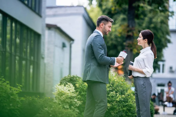 Journalist holding microphone and talking with businesswoman in formal wear — Stock Photo