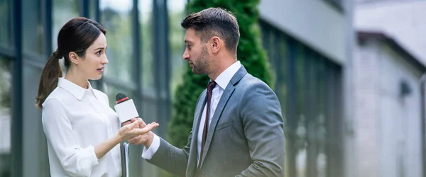 Panoramic shot of journalist holding microphone and talking with businesswoman in formal wear — Stock Photo