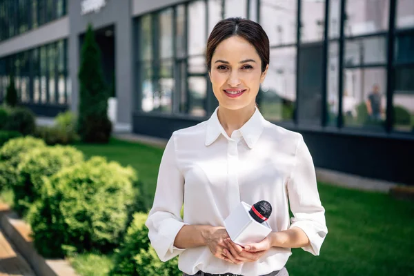 Attractive journalist in formal wear holding microphone and smiling outside — Stock Photo