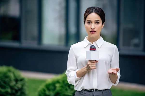Attraktive Journalistin in offizieller Kleidung, die Mikrofon in der Hand hält und draußen spricht — Stockfoto