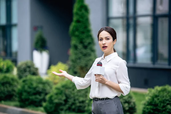 Attractive journalist in formal wear holding microphone and speaking outside — Stock Photo
