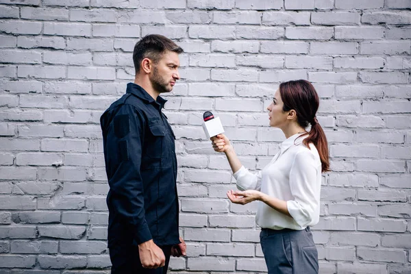 Giornalista che tiene il microfono e parla con un bel poliziotto in uniforme — Foto stock