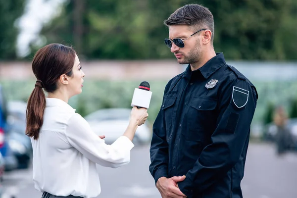 Journaliste tenant un micro et parlant avec un beau policier en uniforme — Photo de stock