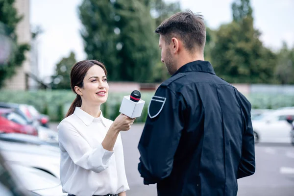 Journaliste tenant un micro et parlant avec un beau policier en uniforme — Photo de stock