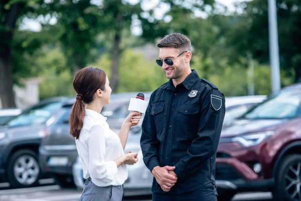 Periodista sosteniendo micrófono y hablando con guapo policía en uniforme - foto de stock