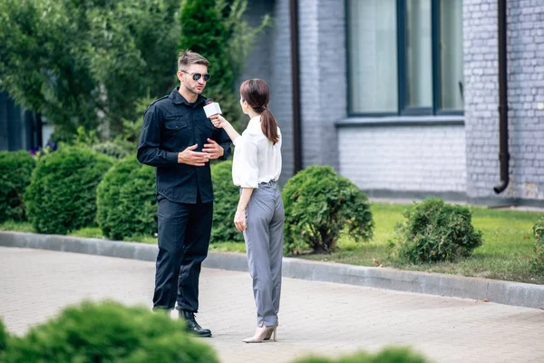 Journaliste tenant un micro et parlant avec un beau policier en uniforme — Photo de stock