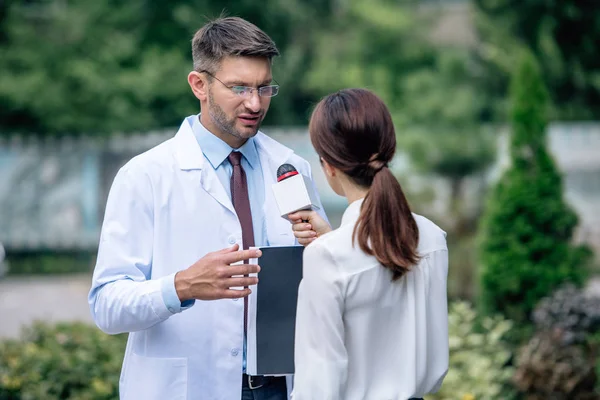 Journalist holding microphone and talking with handsome doctor in white coat — Stock Photo