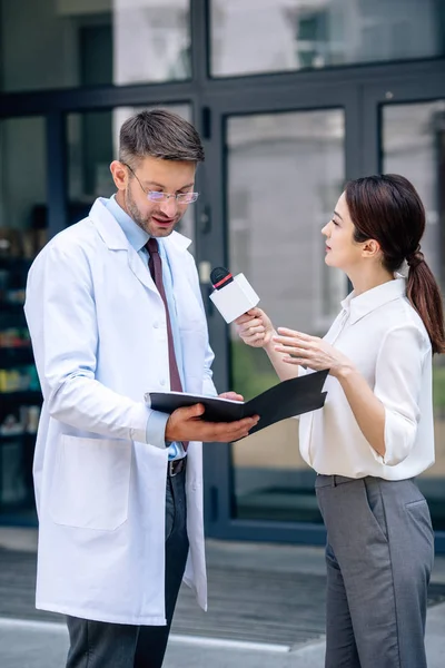 Journalist hält Mikrofon in der Hand und spricht mit hübschem Arzt im weißen Kittel — Stockfoto