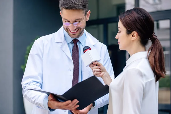 Journalist holding microphone and talking with handsome doctor in white coat — Stock Photo