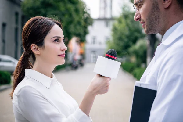 Журналист держит микрофон и разговаривает с красивым доктором в белом халате — стоковое фото