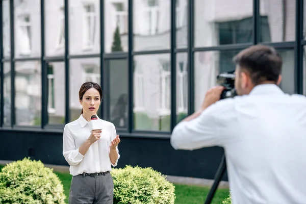 Selektiver Fokus attraktiver Journalistin mit Mikrofon und Kameramann, die sie draußen filmt — Stockfoto