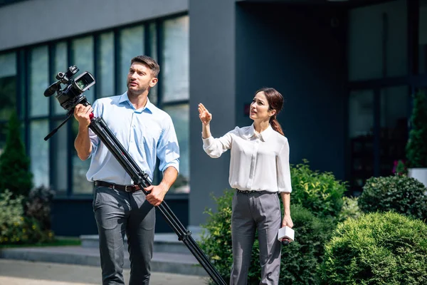 Attraktiver Journalist mit Mikrofon und Kameramann mit digitaler Videokamera — Stockfoto