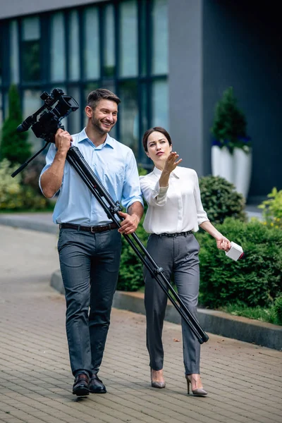 Attrayant journaliste tenant microphone et caméraman tenant caméra vidéo numérique — Photo de stock