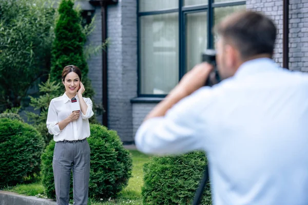 Selective focus of attractive journalist holding microphone and cameraman shooting her outside — Stock Photo