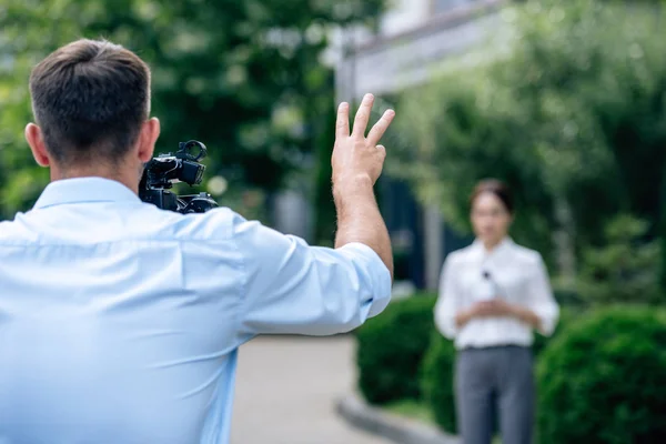 Fuoco selettivo di ripresa cameraman mostrando gesto e ripresa giornalista — Foto stock