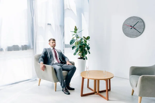 Guapo hombre de negocios en ropa formal y gafas sentado en la oficina - foto de stock