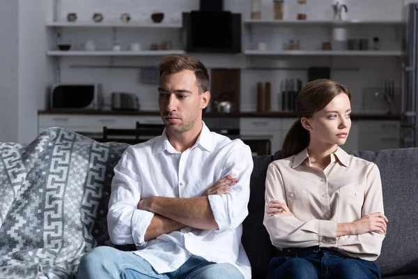 Pensive sad man and woman sitting on sofa with crossed arms — Stock Photo