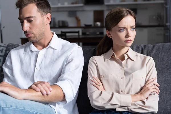 Pensive sad man and woman sitting on sofa with crossed arms — Stock Photo