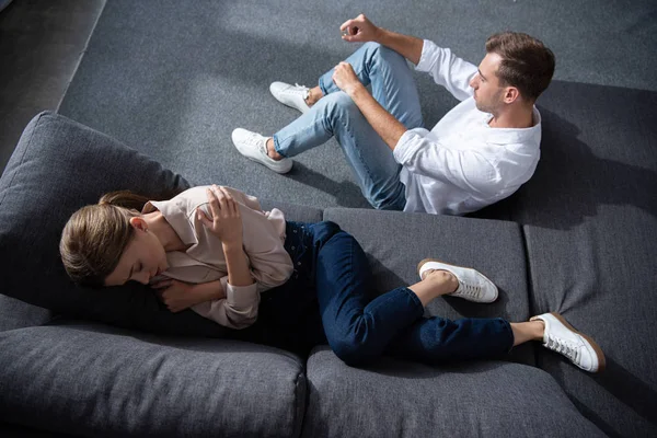 Ansicht der weinenden Frau auf dem Sofa liegend und des Mannes auf dem Boden sitzend — Stockfoto
