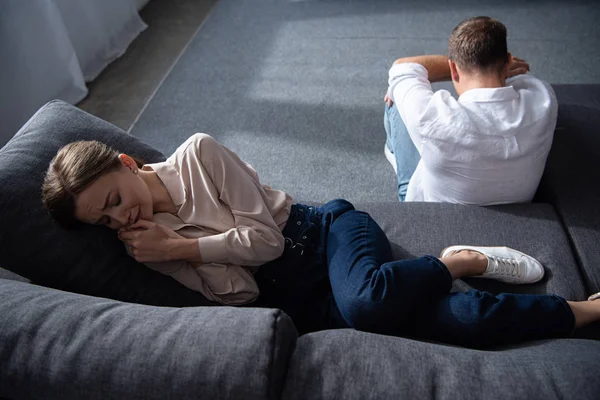 Weinende aufgebrachte Frau auf Sofa und Mann auf dem Boden im Wohnzimmer — Stockfoto