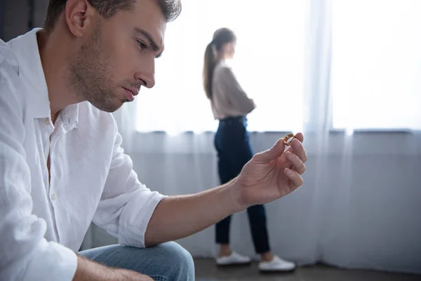 Uomo pensieroso che tiene anello e donna in piedi vicino alla finestra — Foto stock