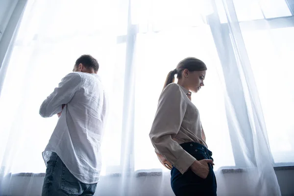 Вид снизу расстроенной женщины и мужчины в рубашках, стоящих у окна — стоковое фото