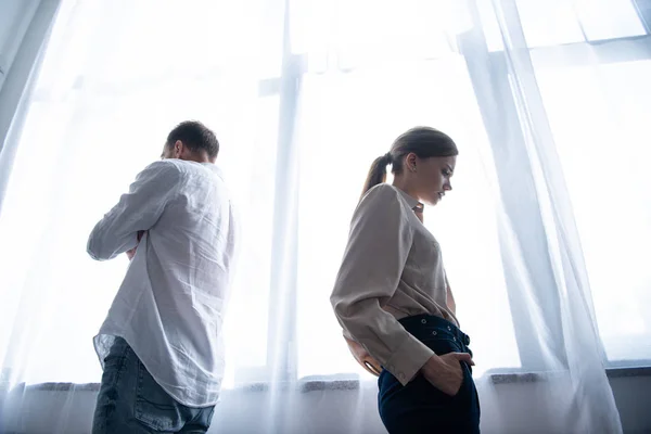 Vista dal basso di donna e uomo sconvolto in camicie in piedi vicino alla finestra — Foto stock