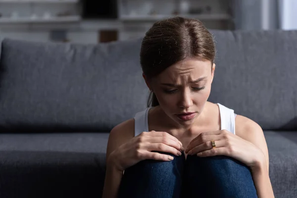 Mujer joven deprimida con anillo sentado cerca del sofá en la sala de estar en casa - foto de stock