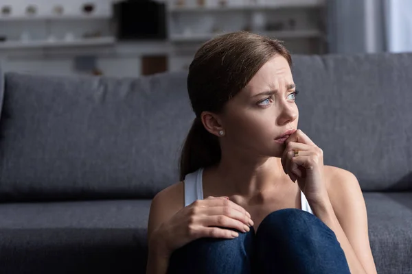 Засмучена молода жінка з кільцем, що сидить біля дивана у вітальні вдома — стокове фото