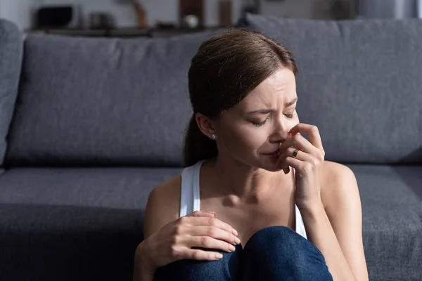 Verärgerte junge Frau mit Ring sitzt neben Sofa und weint zu Hause — Stockfoto