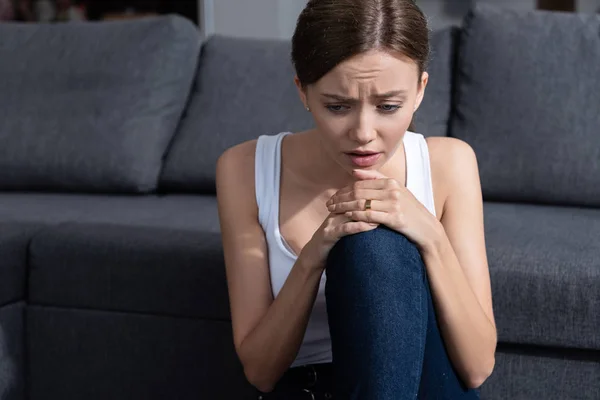 Stressed young woman sitting near sofa in living room — Stock Photo