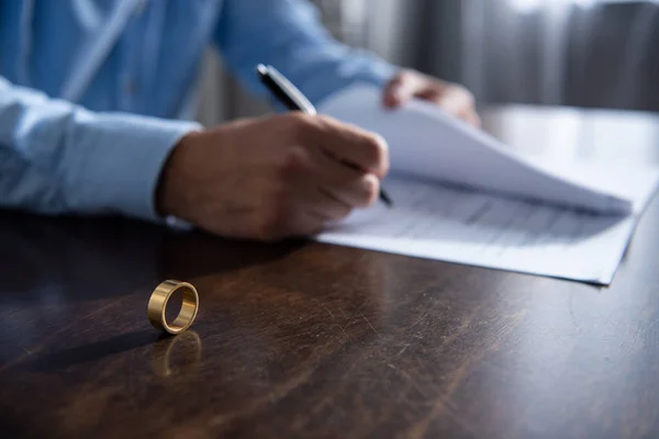 Vista parcial del hombre sentado en la mesa y firmando documentos de divorcio - foto de stock