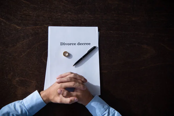 Partial view of man sitting at table with clenched hands with divorce documents — Stock Photo