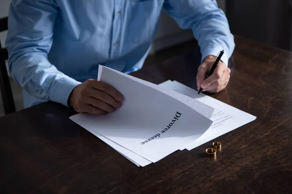 Visão parcial do homem sentado à mesa e assinando documentos de divórcio — Fotografia de Stock