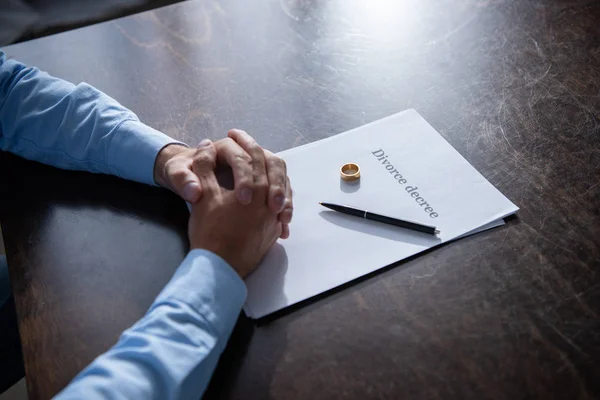 Vista parcial del hombre sentado en la mesa con las manos cerradas con documentos de divorcio - foto de stock